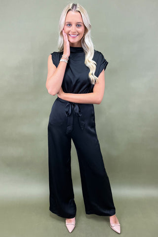 Woman wearing a black jumpsuit against a green background