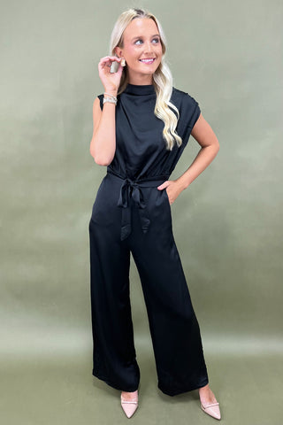 Woman wearing a black jumpsuit against a green background