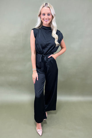 Woman wearing a black jumpsuit against a plain background