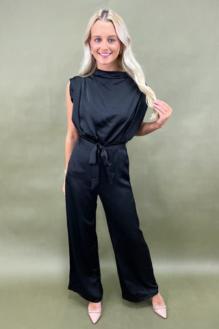 Woman wearing a black jumpsuit against a green background