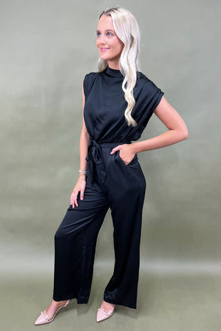 Woman wearing a black jumpsuit against a plain background