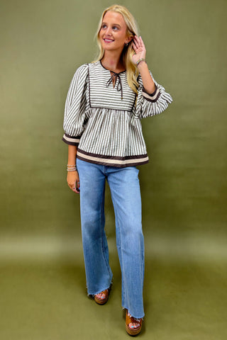 Woman wearing a striped blouse and blue jeans against a green background