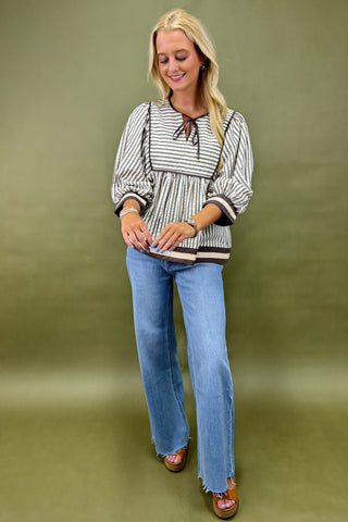 Woman wearing a striped blouse and blue jeans against a green background
