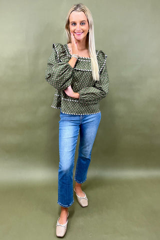 Woman wearing a green patterned blouse and blue jeans against a green background