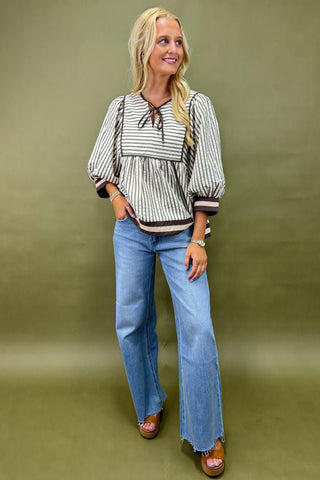 Woman wearing a striped blouse and blue jeans against a green background