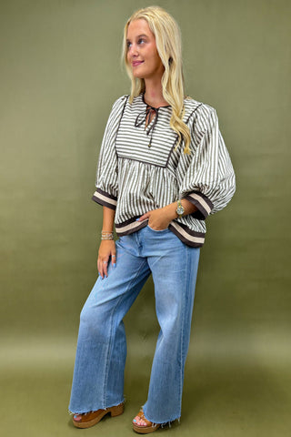 Woman wearing a striped blouse and blue jeans against a green background