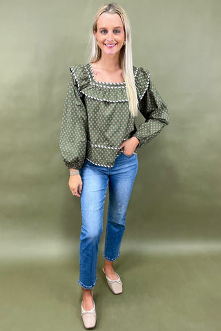Woman wearing a green patterned blouse and blue jeans on a green background