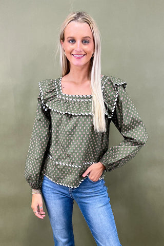 Woman wearing a green polka dot blouse with ruffled sleeves against a green background