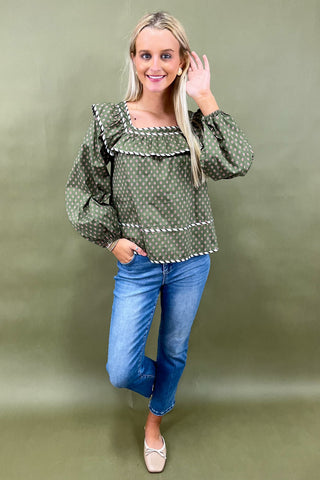 Woman wearing a green patterned blouse and blue jeans against a green background