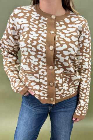 Person wearing a brown and white patterned cardigan with blue jeans on a green background