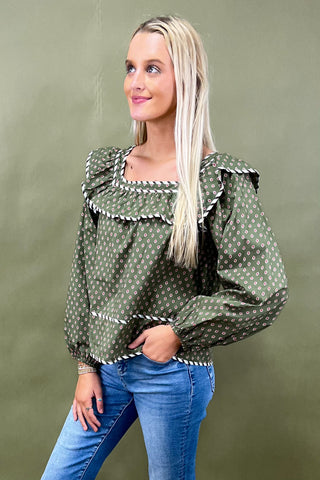 Woman wearing a green patterned blouse with blue jeans against a green background