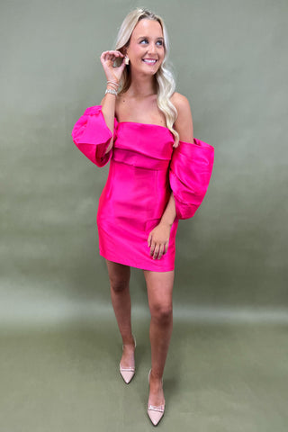 Woman wearing a bright pink off-shoulder dress with ruffled sleeves against a green background