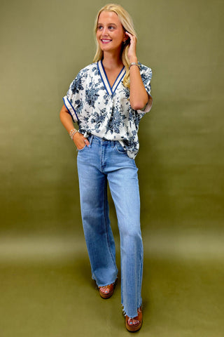 Woman wearing a floral blouse and blue jeans against a green background