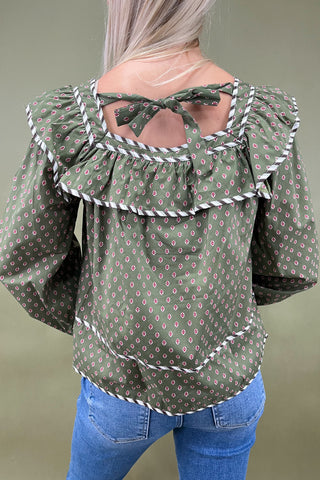 Green patterned blouse with ruffled sleeves worn by a person against a neutral background