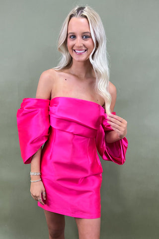 Woman wearing a bright pink off-shoulder dress against a plain background