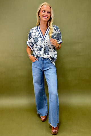 Woman wearing a floral blouse and blue jeans against a green background