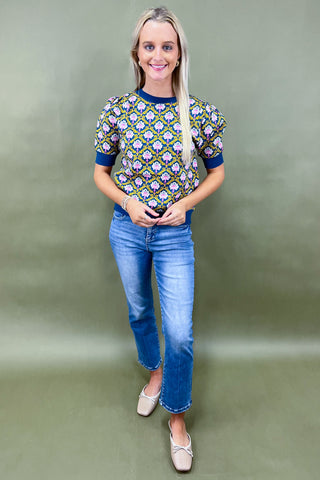 Woman wearing a patterned top and blue jeans against a plain background