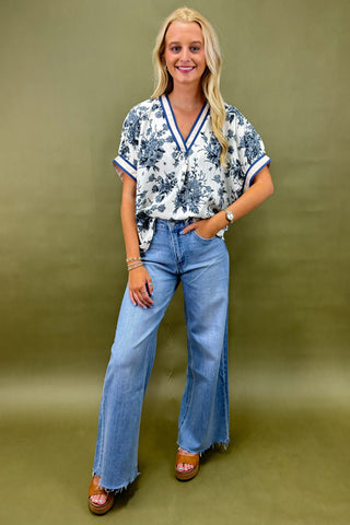Woman wearing a floral blouse and blue jeans against a green background