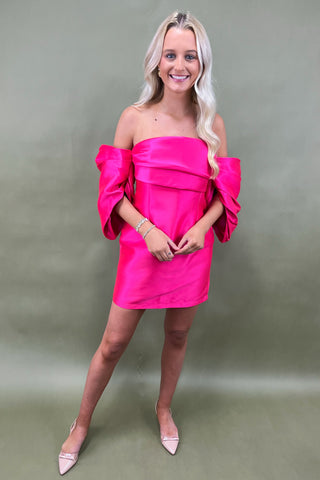 Woman wearing a bright pink off-shoulder dress against a plain background