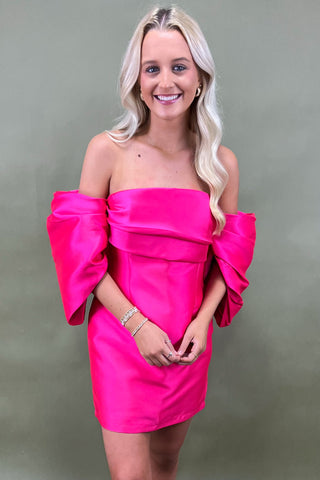 Woman wearing a bright pink strapless dress against a plain background