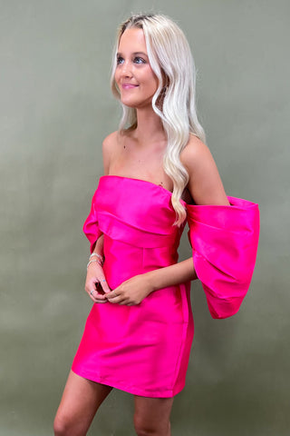 Woman wearing a bright pink strapless dress with puffed sleeves against a plain background