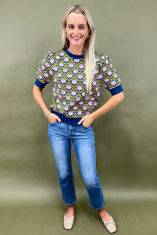 Woman wearing a patterned top and blue jeans against a green background