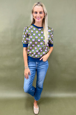 Woman wearing a patterned top and blue jeans against a green background
