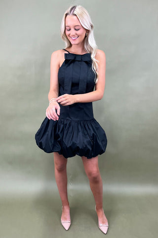 Woman wearing a black dress with a bow detail on a plain background