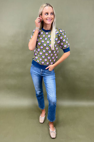 Woman wearing a patterned top and jeans against a green background
