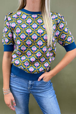 Woman wearing a patterned top with blue jeans against a green background