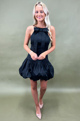 Woman wearing a black dress with a large bow on a plain background