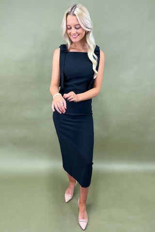 Woman wearing a black sleeveless dress against a green background