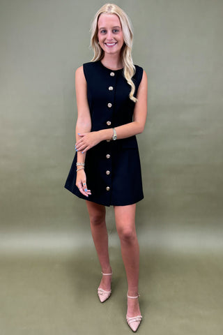 Woman wearing a black dress with buttons on a plain background