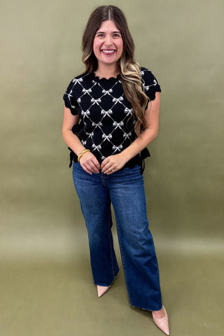 Woman wearing a black top with white patterns and blue jeans on a green background