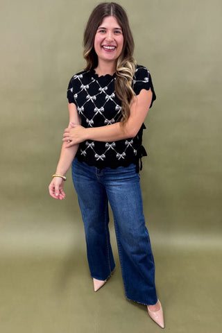 Woman wearing a black top with white patterns and blue jeans on a green background