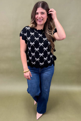 Woman wearing a black top with white patterns and blue jeans on a green background