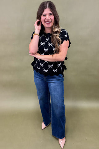 Woman wearing a black patterned top and blue jeans against a green background