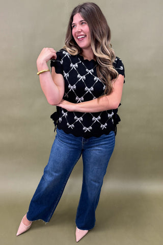 Woman wearing a black top with white patterns and blue jeans on a beige background