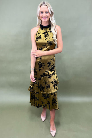 Woman wearing a gold and black floral dress against a plain background