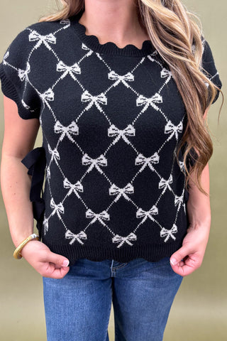 Person wearing a black sweater with white bow pattern and blue jeans against a beige background