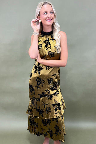 Woman wearing a gold dress with black floral patterns against a plain background