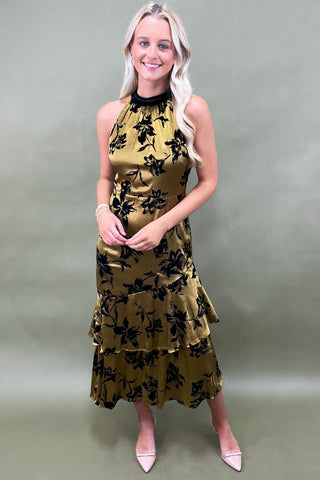 Woman wearing a gold dress with black floral patterns against a plain background