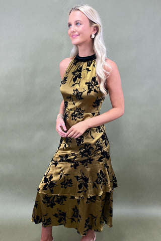 Woman wearing a gold dress with black floral patterns against a plain background