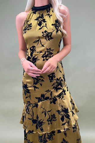 Woman wearing a mustard yellow dress with black floral pattern on a plain background