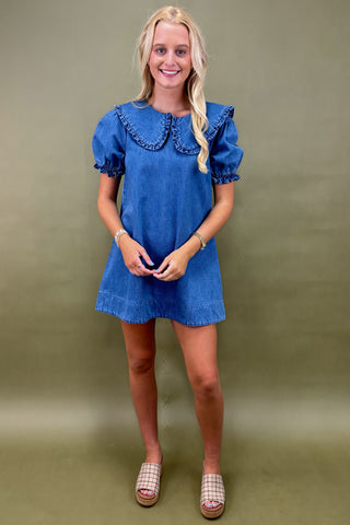 Woman wearing a blue dress with ruffled collar against a green background