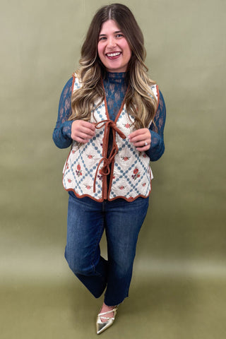 Woman wearing a patterned vest over a blue top and jeans on a green background