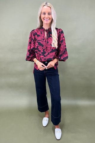 Woman wearing a red floral blouse and dark jeans against a plain background