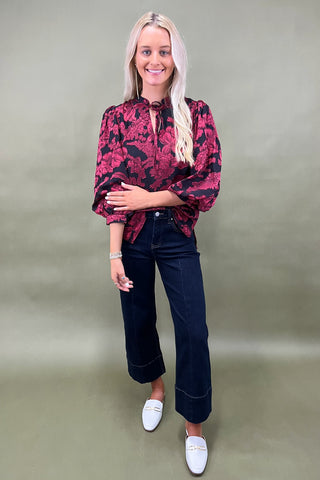 Woman wearing a red floral blouse and dark jeans against a plain background