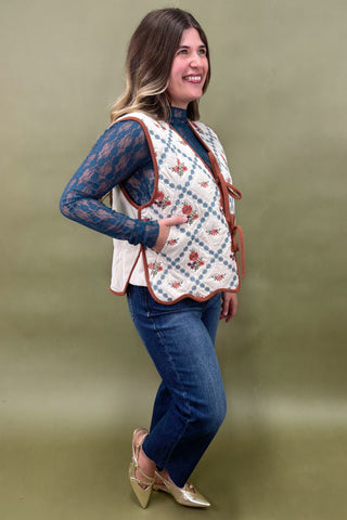 Woman wearing a patterned vest over a blue top and jeans on a green background