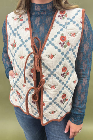 Quilted vest with floral embroidery and brown trim worn over a blue lace top and jeans.